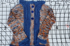 Hand-knit infant sweater with solid denim blue and blue/orange yarn in alternating areas and blue buttons.