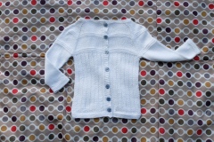 Hand-knit infant sweater in white yarn and slate blue buttons.